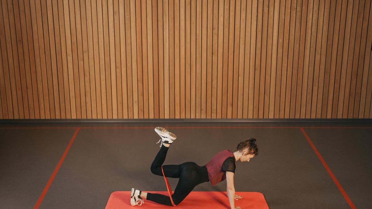 Woman performing a resistance band workout on a mat indoors, focusing on fitness and strength.